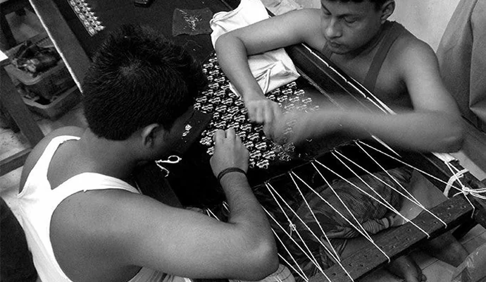 Two karigars working embroidery on a stretched frame
