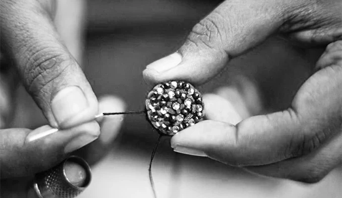 Hands threading a needle through a mirror-work button